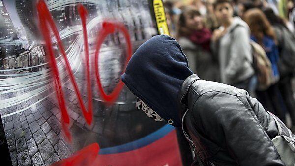 Maskierter Demonstrant besprüht ein Plakat bei Ante-Expo-Protest